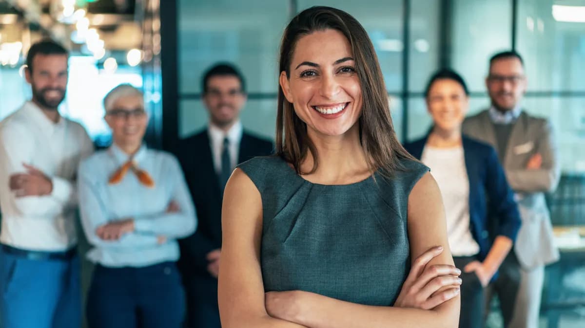 Selbstbewusste Managerin mit verschränkten Armen vor ihrem Team in einem hellen Büro – Symbolbild für professionell begleitete Freiwilligenprogramme im Personalabbau